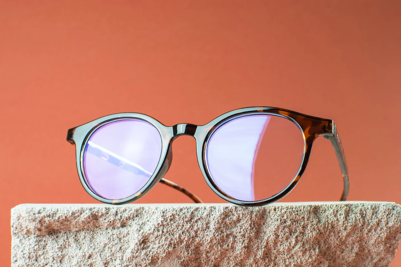 Monturas de gafas vintage exclusivas en Almería con lentes violetas sobre fondo terracota